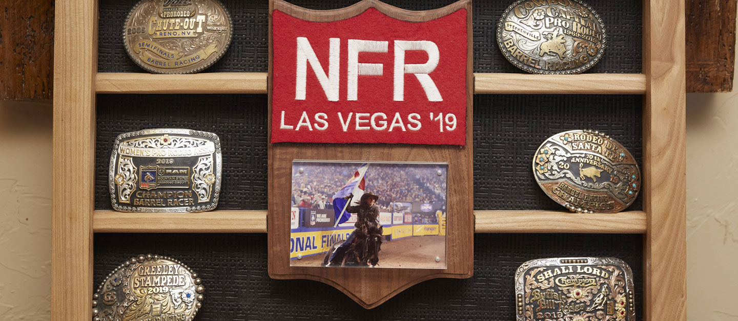 Shali lord’s buckle display with her NFR back number and a photo of her running barrels on her horse all hanging on the wall.